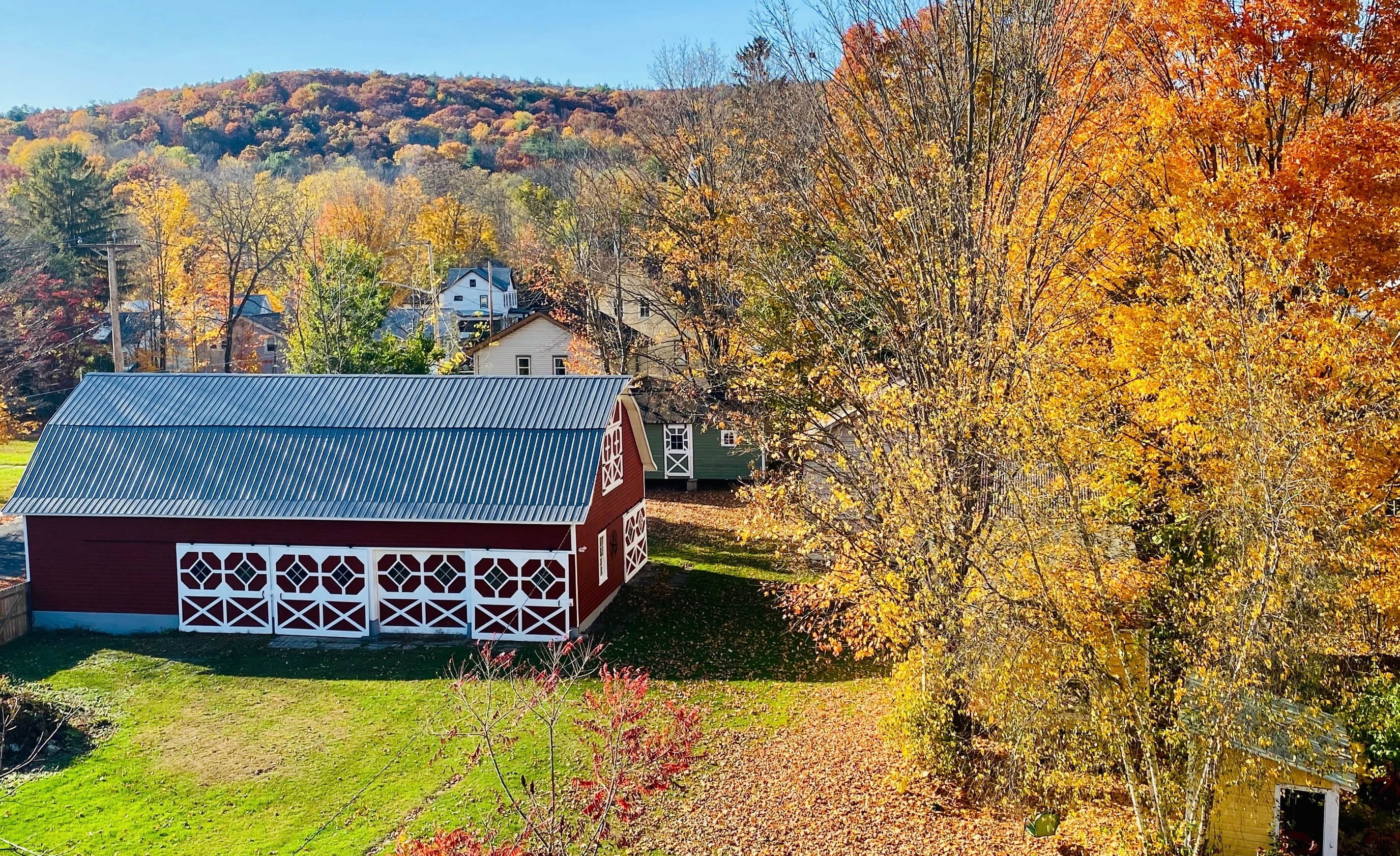 Completed barn restoration — new metal roof, fresh red paint, and white trim in autumn landscape