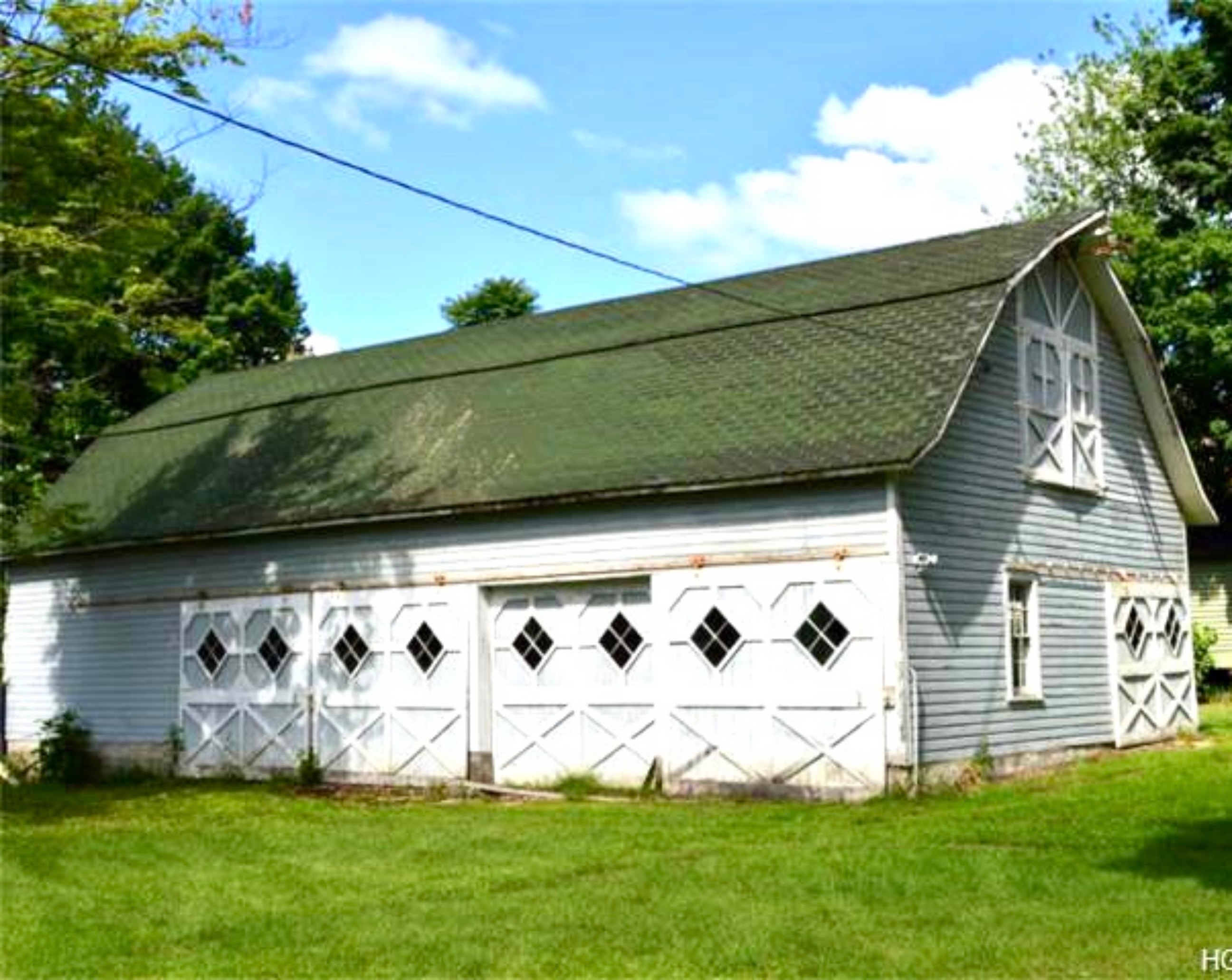 Historic barn before restoration — worn asphalt shingle roof and faded white siding
