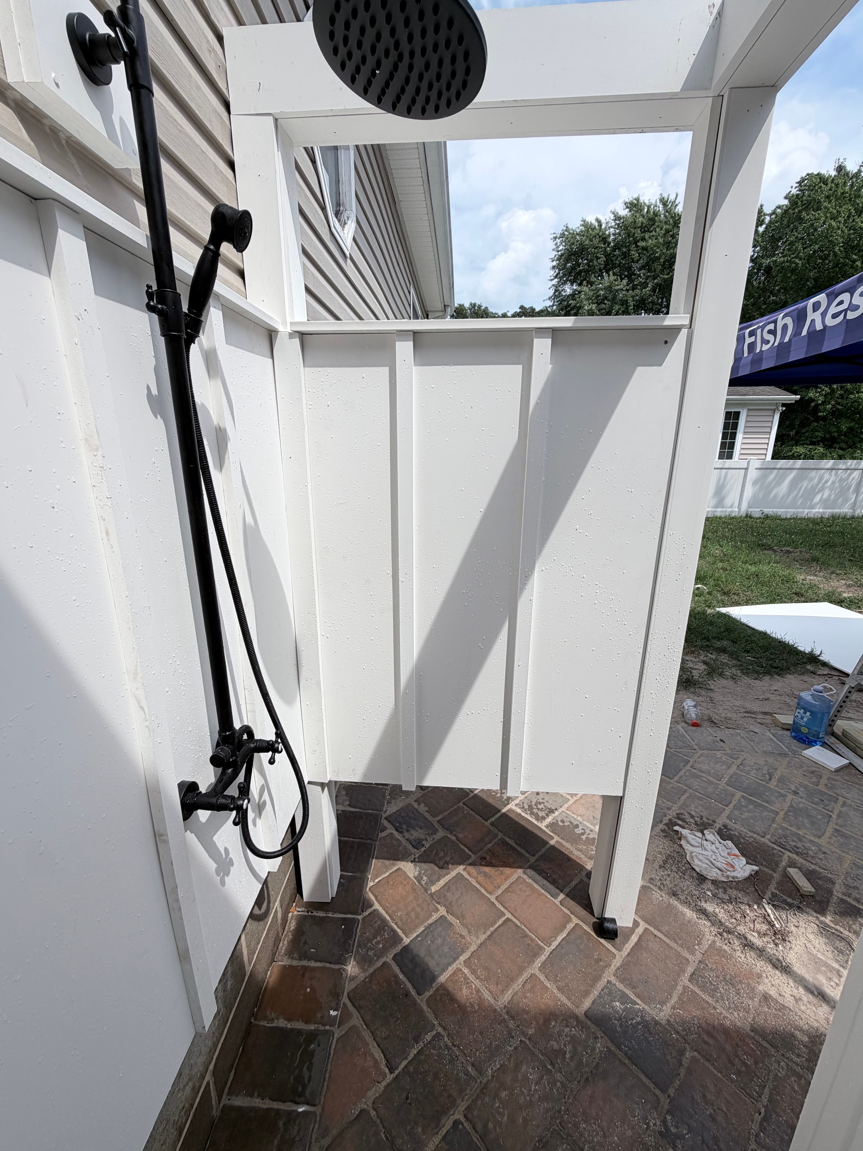 Murray Brothers outdoor shower build — white PVC enclosure with black plumbing fixtures and showerhead