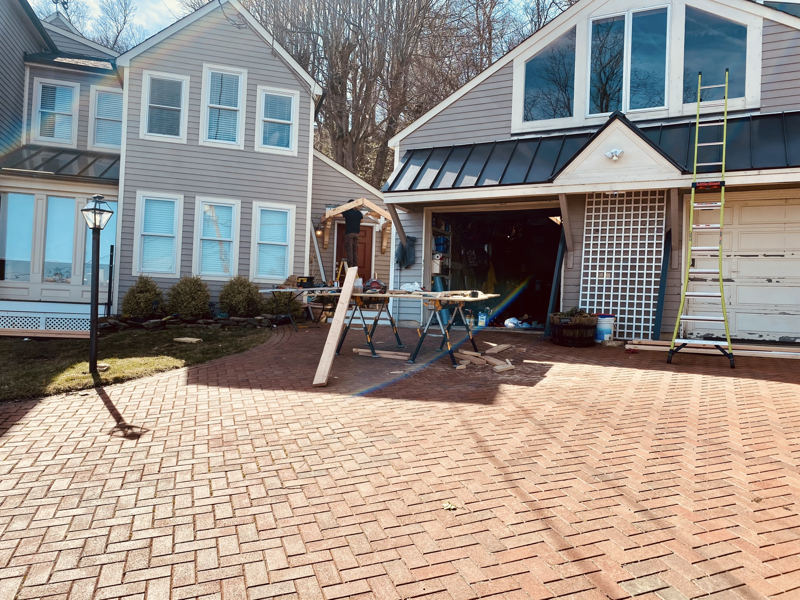 Completed standing seam metal roof on residential garage with brick paver driveway, crew finishing trim work