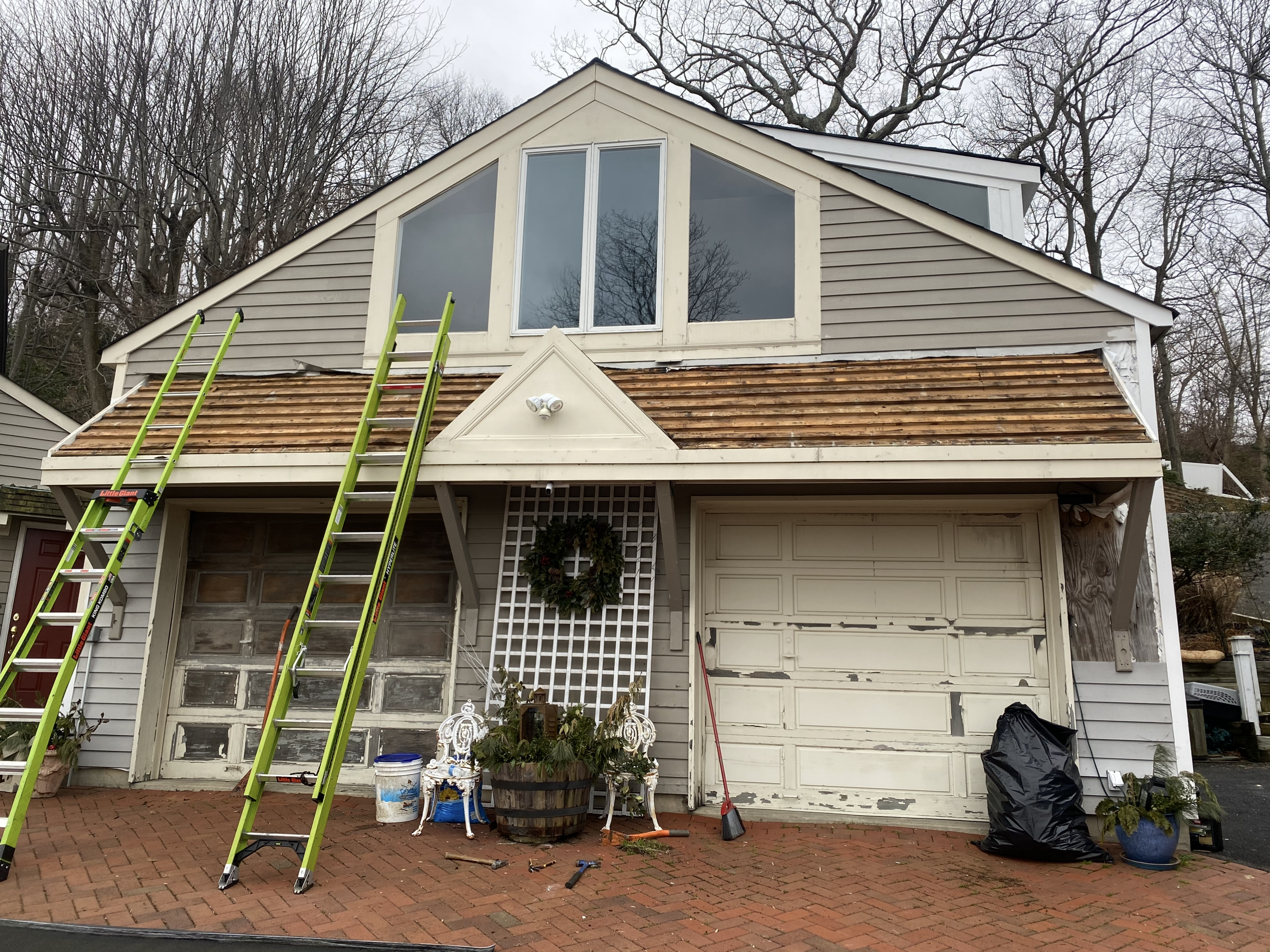 Residential garage with old cedar shake roof stripped down to deck boards, ladders staged for metal roof installation