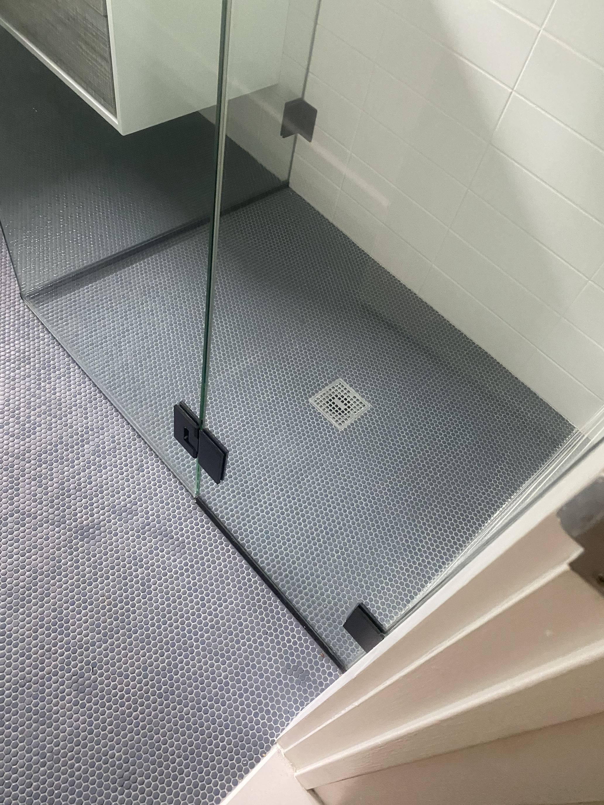 Modern glass shower enclosure with gray penny tile floor and white subway tile walls